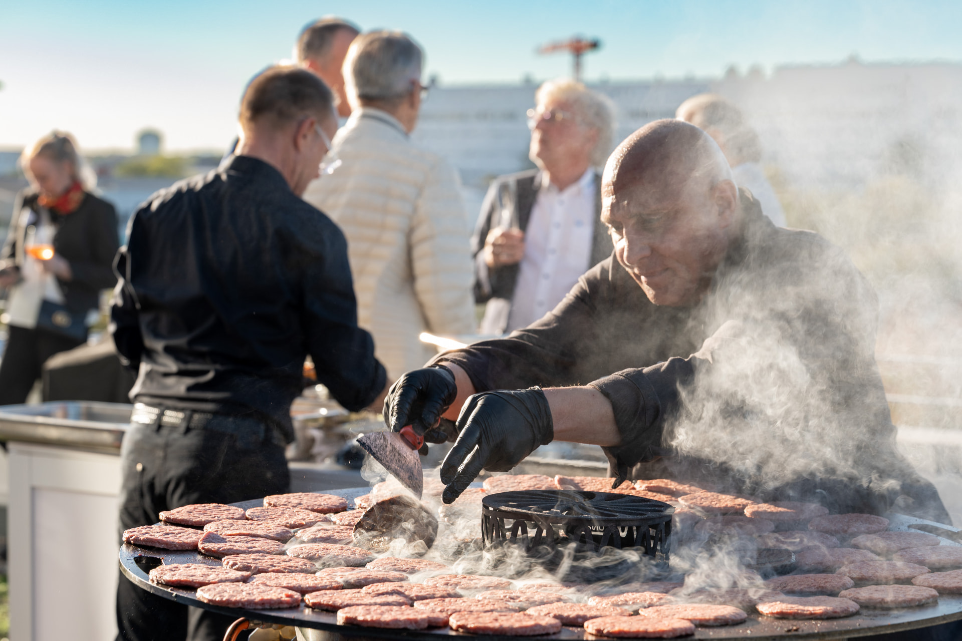 Der Koch wendet Burger-Pattys auf der Grillplatte mit viel Rauch