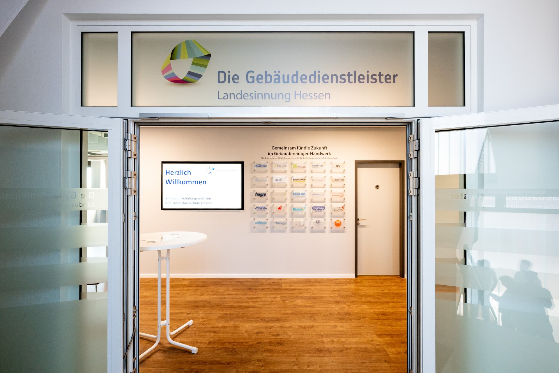 Eingang zum Schulungszentrum mit Bildschirm „Herzlich Willkommen“
